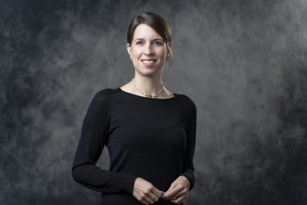 Bewerbungsfoto einer Frau im schwarzen Oberteil vor dunklem Studiohintergrund