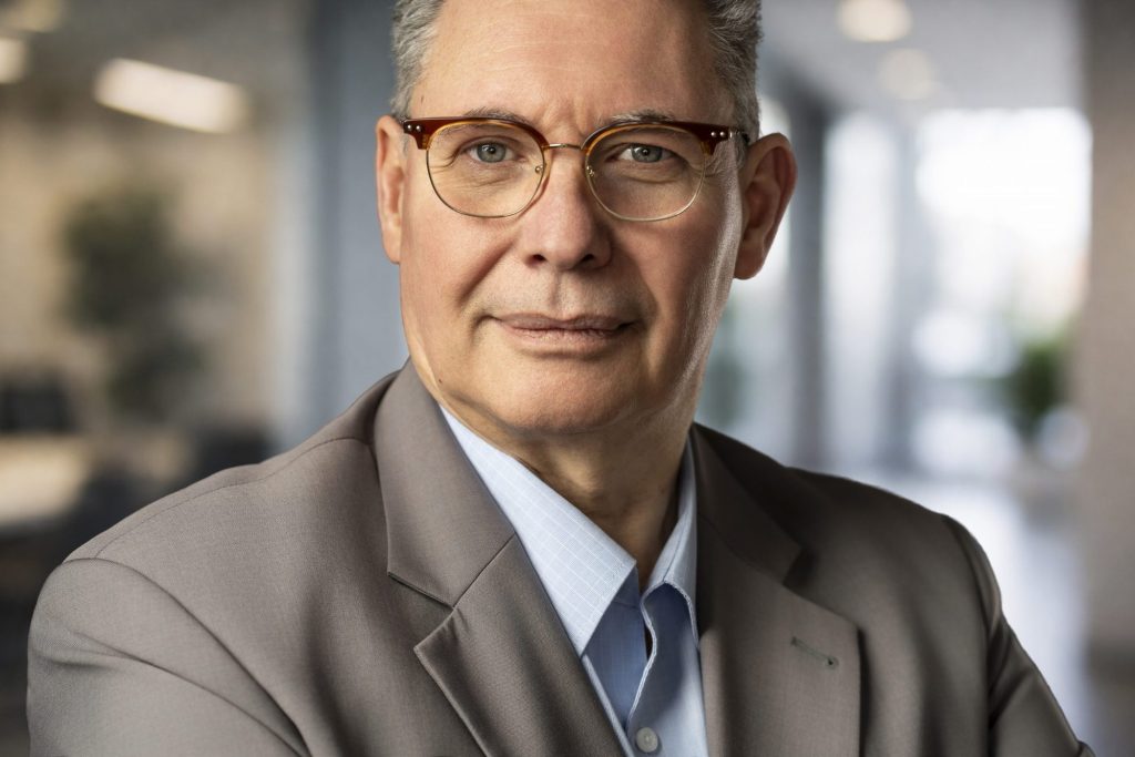 Bewerbungsfoto eines älteren Mannes mit Brille im beigen Anzug vor Bürohintergrund – Bewerbungs- und Businessfotos in Karlsruhe