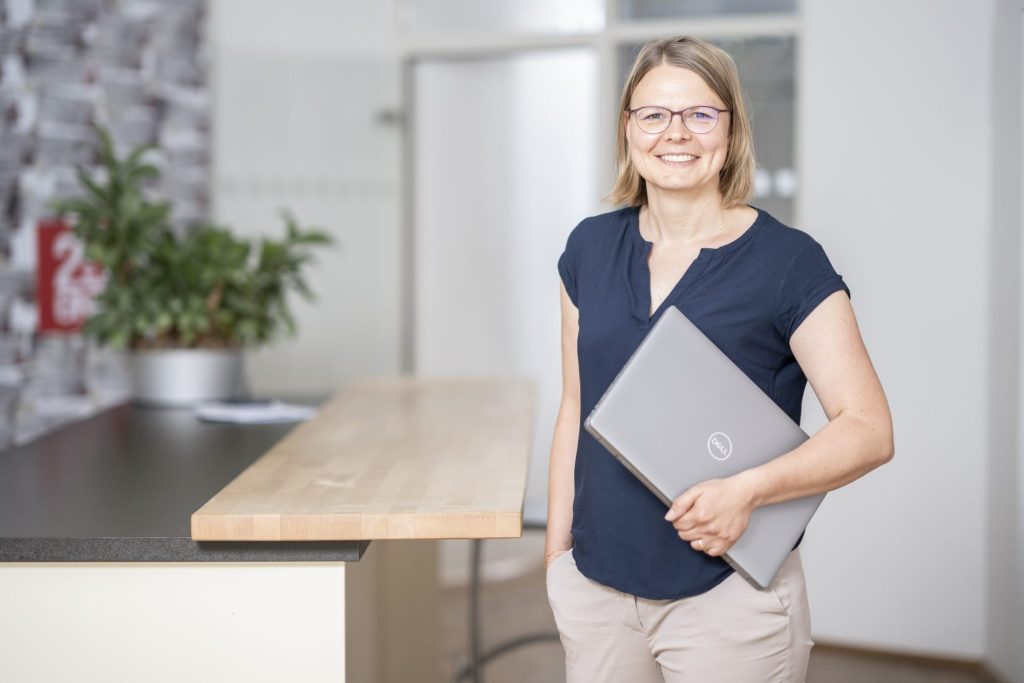 Mitarbeiterportrait einer Frau mit Laptop im hellen Büro – Portrait im Arbeitsumfeld
